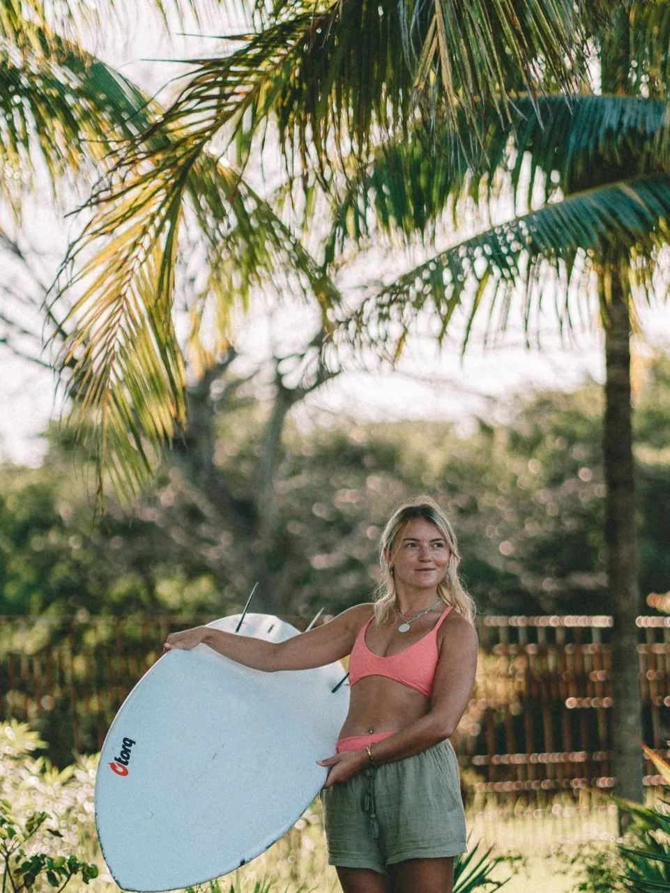 Sophie Deakin with her surfboard under the palms
